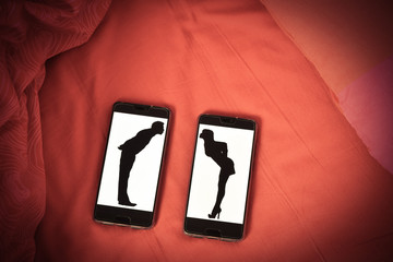 deux silhouette d'amoureux qui tentent de s'embrasser sur des téléphones posés sur les draps...