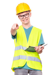 Funny Handsome Teen Boy wearing Safety Jacket and yellow Hard Hat. Portrait of Happy Child with notebook and pen, is Pointing Finger on You, isolated on white background.