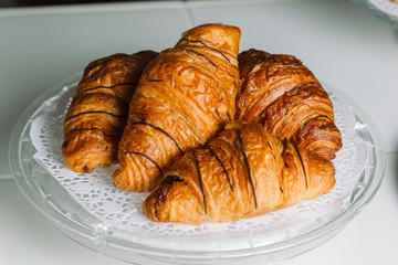 Fresh croissants on round plate on white wooden table.