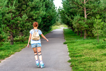 Sporting girl rollerscating in park fir alley on summer day.