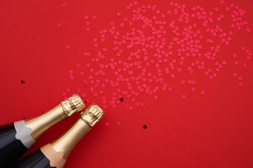 Champagne bottles with confetti hearts on red background. Copy space, top view