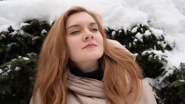 Portrait of a beautiful young girl in a jacket on the background of snow and pine branches.