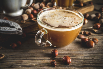 Homemade hazelnut coffee latte or cappuccino, rustic wooden background with hazelnuts, three coffee...