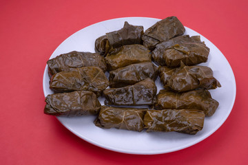 Middle Eastern Vegetarian Dolma, stuffed grape leaves with rice on white dish on red surface.