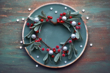 Red mistletoe Christmas wreath on round decorative tray on matching textured background