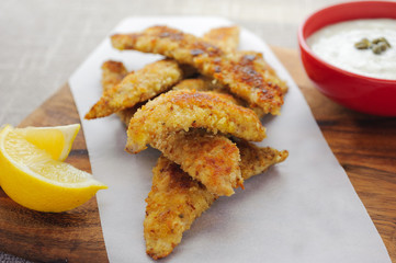 Crumbed fish served with lemon and homemade tartare sauce in background, selective focus with copy space