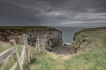 Fototapeta premium Limestone quarry on Pembrokeshire coast, Uk.Cliff top with fence and moody sky above sea.Landscape scene with copy space.