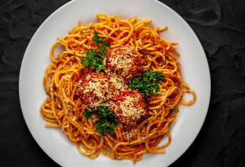 Italian pasta with tomato sauce and meatballs in a white plate, dark background