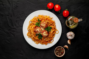 Italian pasta with tomato sauce and meatballs in a white plate, dark background