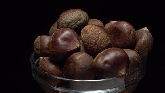 Chestnut. Close up. Heap of raw unroasted sweet chestnut in a bowl in rotation. Food background. black background, studio shot. Healthy food diet concept. Gastronomy and organic food concept