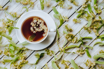 White cup of linden tea on linden blossom background. Herbal medicine. Top view. Treatment of cold and flu concept.