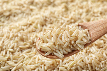Wooden spoon with raw brown rice over cereal, closeup