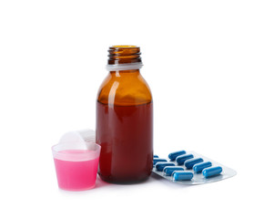 Measuring cup and bottle of cough syrup with pills on white background