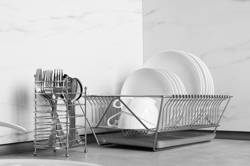 Drying rack with clean dishes near cutlery holder on table in kitchen