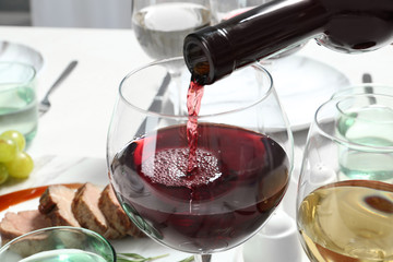 Pouring red wine into glass on table, closeup