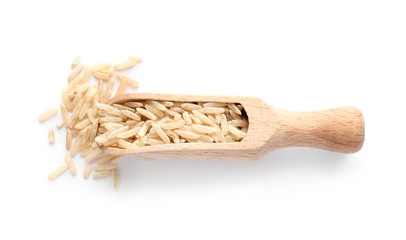 Scoop with uncooked brown rice on white background, top view