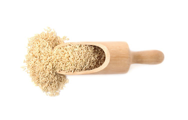 Scoop with uncooked brown rice on white background, top view
