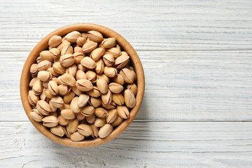 Organic pistachio nuts in bowl on wooden table, top view. Space for text