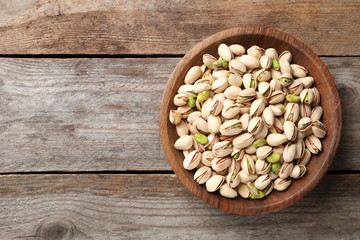 Organic pistachio nuts in bowl on wooden table, top view. Space for text