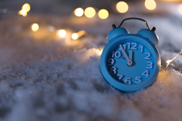 Alarm clock and Christmas lights on white snow outdoors, space for text. Midnight countdown