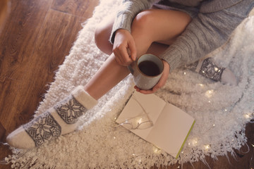 Fototapeta na wymiar Woman with cup of hot beverage and book at home in winter evening, closeup
