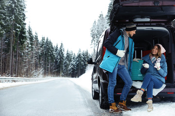 Couple near open car trunk full of luggage on snowy road, space for text