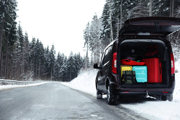 Car with open trunk full of luggage near snowy road in forest