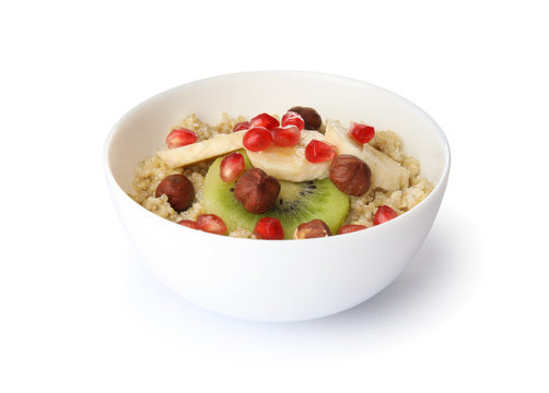 Bowl of quinoa porridge with hazelnuts, kiwi, banana and pomegranate seeds on white background