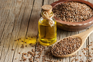 Heap of Flax seeds or linseeds in spoon and bowl with glass of linseed oil on wooden backdrop....