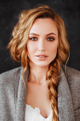 Fototapeta premium Beautiful smiling blonde woman model in stylish dark overcoat and white dress on dark gray background