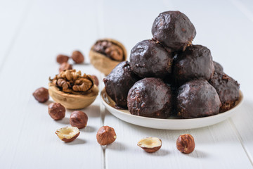 Chocolate-drenched balls of grated nuts and dried fruits in a bowl and walnuts on a rustic light table.