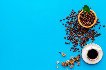 Brown roasted coffee beans scattered on blue background and cup of americano top view mockup