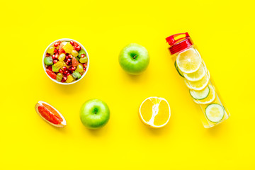 Weight loss concept. Fruit salad near fruit lemon and cucumber water on yellow background top view