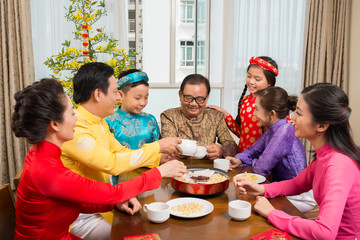 Happy big Asian family in traditional costumes drinking tea and celebrating Lunar New Year