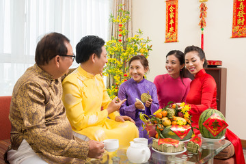 Happy Asian family enjoying fresh fruits at Chinese New Year celebration at home with couplets with best wishes for coming year in background