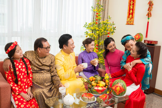 Happy Asian family drinking tea and eating fresh fruits at Lunar New Year celebration with couplets with best wishes for coming year in background