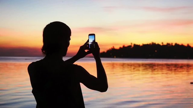 Silhouette of young man takes picture with mobile phone on a background of beautiful sunset. slow motion. 1920x1080