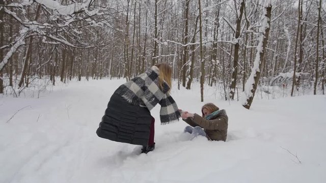 two funny girlfriends fool around in the winter in the forest, lying in snow drifts.