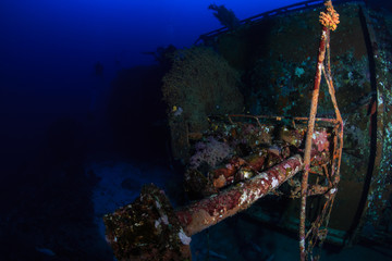 SCUBA divers exploring a deep, underwater shipwreck in a clear, tropical ocean