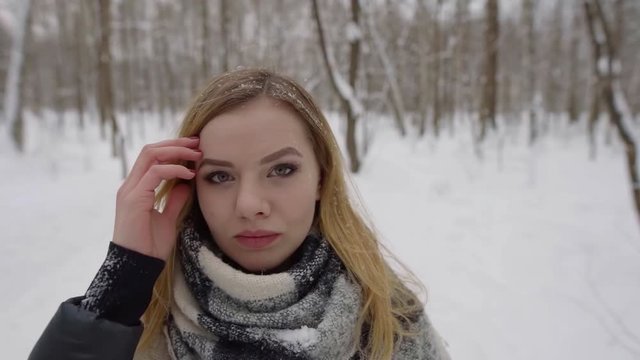 portrait of a beautiful light girl close-up in the winter on the street. On the background of snowy forest, her hair of the snowflakes.