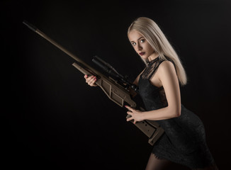 Fototapeta premium young blonde girl in black dress posing on black background with weapon