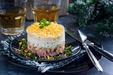 Salad in layers with canned mushrooms, smoked chicken and cheese on a black plate, horizontal