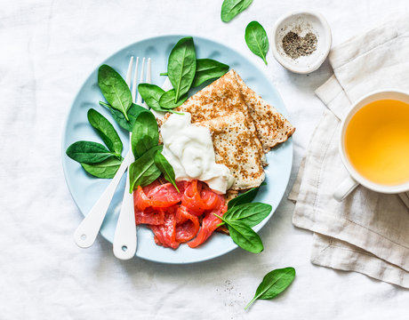 Delicious Breakfast Or Brunch - Crepes With Smoked Salmon, Spinach And Sour Cream On A Light Background, Top View