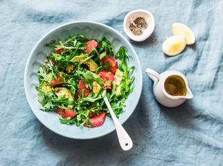 Avocado, grapefruit, rocket salad with mustard olive oil salad dressing on blue background, top view. Vegetarian diet food concept