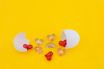 White shell (broken egg), from which many small hearts were poured on a yellow background. The birth of love. Broken heart.  Cook love from ingredients