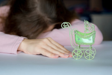 A pose of despair, a loss of hope. A woman lies face down on a table, with cancer reaching for a toy baby carriage. The stroller in the foreground is in focus, the woman is blurred. 