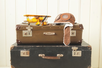 Helmet pilot and toy yellow metal plane Two old retro suitcases White wooden background Vintage tinting Copy space