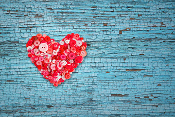 Red heart of many buttons on a blue wooden background with cracked paint on the left.