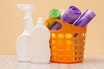 Bottles of dishwashing liquid, basket with garbage bags and sponges on wooden desk.