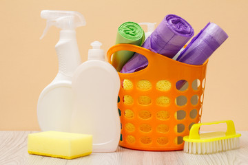 Bottles of dishwashing liquid, basket with garbage bags and sponges on wooden desk.